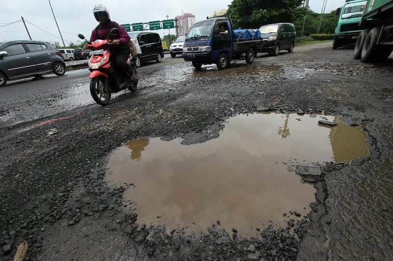 Kendaraan melaju perlahan saat melintasi jalan yang rusak parah. (Foto:MI/Immanuel)